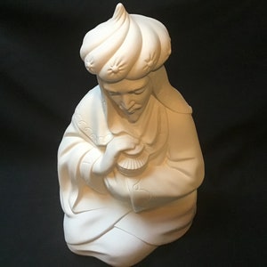 May include: White ceramic figurine of a kneeling man wearing a turban and holding a small box. The figurine is a traditional Christmas decoration.