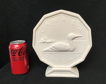 May include: White ceramic replica of a Canadian dollar coin featuring a loon bird and the words "CANADA" and "DOLLAR".