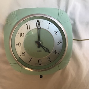 May include: A vintage green electric clock with a white face and black hands. The clock has a silver rim and the text "Smiths Electric" is printed on the face.