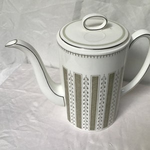 May include: White ceramic coffee pot with a black and green geometric pattern. The pot has a lid with a silver trim.
