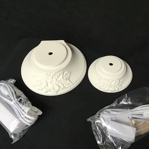 May include: Two white ceramic bases with a holly leaf design, one larger than the other, and two white electrical cords with plugs.