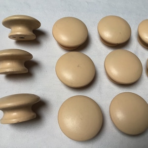 May include: A collection of 11 round, beige wooden knobs with a smooth finish. The knobs are arranged in a semi-circle pattern on a white surface.