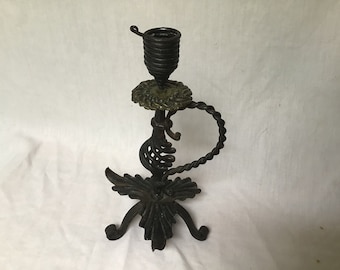 Puede incluir: Un candelero de metal negro con un diseño retorcido y una base decorativa. El candelero tiene una parte superior redonda y abierta para sostener una vela.