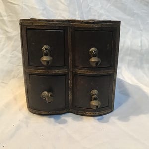Peut inclure: Un coffret à bijoux en bois brun foncé à quatre tiroirs avec des accents en laiton. Chaque tiroir a une tirette décorative en laiton. La boîte a une forme incurvée unique et est probablement vintage.