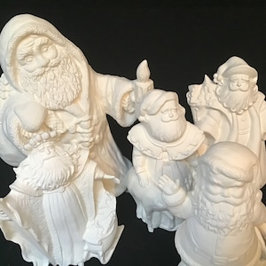 Puede incluir: Un conjunto de cuatro figuras de Papá Noel de cerámica blanca. Las figuras están todas en diferentes poses y tienen diferentes expresiones faciales. Un Papá Noel sostiene una bolsa de regalos, otro sostiene una vela y otro sostiene un saco de juguetes. El cuarto Papá Noel está de pie con los brazos cruzados.