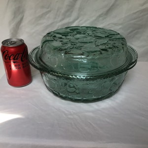 May include: A green glass casserole dish with a lid. The dish has a floral design and is approximately 20 cm in diameter.