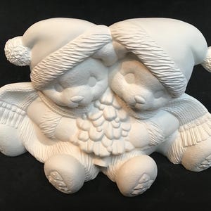 May include: Two white ceramic bears wearing winter hats and scarves, holding a pine cone Christmas tree. The bears are facing each other and have a sweet expression on their faces.
