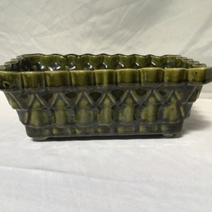 May include: A green ceramic planter with a decorative design. The planter has a rectangular shape and a scalloped rim.