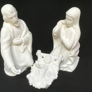 May include: White ceramic figurine set depicting the Nativity scene. The figures include Joseph, Mary, and baby Jesus in a manger.