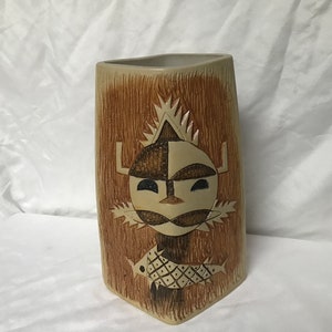 May include: A ceramic vase with a brown and beige design. The vase features a stylised face with geometric patterns and a fish below it.