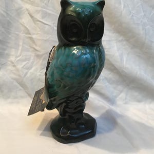 May include: A ceramic owl figurine with a glossy teal and black finish. The owl has large, dark eyes and a detailed feather design. A tag hangs from the side. The figurine is approximately 20 cm tall.