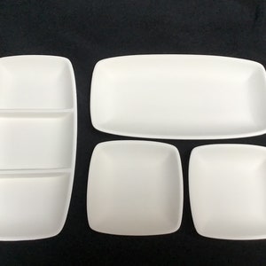 May include: Set of four white ceramic serving dishes. The set includes a rectangular dish with two dividers, a larger rectangular dish, and two square dishes.