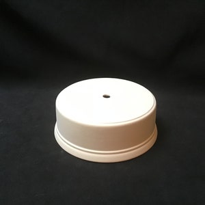May include: A white round cake stand with a single ring around the base. The stand has a small hole in the centre of the top.