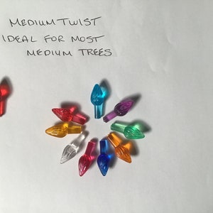 Peut inclure: Assortiment de dix embouts de lampes de Noël en plastique de couleur. Les embouts sont de différentes couleurs, notamment rouge, orange, jaune, vert, bleu, violet et transparent. Le texte "MEDIUM TWIST IDEAL FOR MOST MEDIUM TREES" est écrit à l'encre noire sur fond blanc.