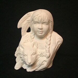 Puede incluir: Busto de cerámica blanca de una niña nativa americana con trenzas largas sosteniendo un cachorro de lobo. La niña lleva un tocado de plumas.