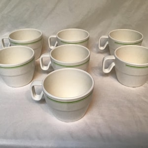 May include: Set of seven white ceramic mugs with a green stripe around the top.