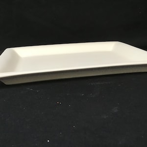 May include: A rectangular, off-white serving tray with a slightly raised edge. The tray has a simple, minimalist design and is suitable for serving appetizers or small dishes. The tray is made of a solid material and is set against a dark background.