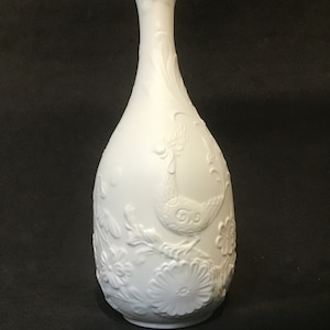 Może przedstawiać: Biały wazon z porcelany z wytłoczonym wzorem kwiatowym i ptakiem. Wazon ma wąską szyjkę i szeroką, zaokrągloną podstawę.
