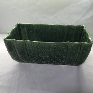 May include: A green ceramic planter with a scalloped rim and a textured, scale-like pattern. The planter is rectangular in shape and has a wide, shallow base.