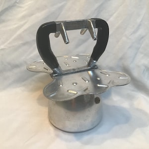 May include: A vintage aluminium stovetop espresso maker with a black handle. The coffee pot has a round base and a flower-shaped top with several holes. The handle is curved and made of black plastic.