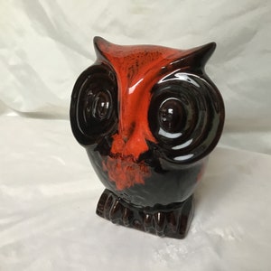 May include: A ceramic owl ornament with a glossy finish. The owl features a striking colour scheme of red, black, and brown. The eyes are large and circular, and the overall design is stylized. This decorative owl is a unique home decor item.