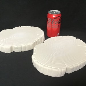 May include: Two white ceramic tree stump coasters. The coasters are shaped like tree stumps with rings and bark details. The coasters are approximately the size of a can of soda.