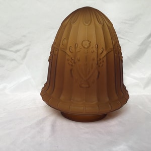 May include: A brown glass lampshade with a decorative floral design. The shade has a fluted texture and a rounded top.