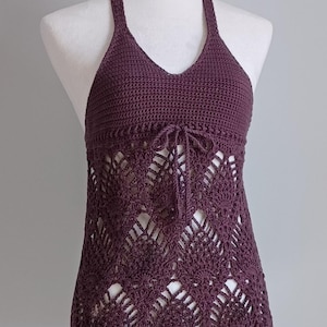 May include: A plum-colored halter top made of crochet. The top features a V-neckline and a drawstring detail at the waist. The lower portion of the top has an open, lacy design. The garment is displayed on a white mannequin.