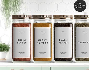 May include: Four glass jars with metal lids filled with spices. The jars are labelled with white labels that say "MBC Kitchen" and the name of the spice: "Chili Flakes", "Curry Powder", "Black Pepper", and "Oregano".