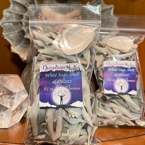 May include: Two clear plastic bags filled with white sage, shell, and quartz incense. The bags are labeled "Quantum Mystics White Sage, Shell & Quartz 1/2 oz. Low Incense".