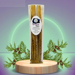 May include: A package of 12 incense sticks with a label that reads "Quantum Mystics Frankincense, Cedar & Juniper Berries 12 Premium Handmade Incense Sticks". The sticks are a golden color and are wrapped in clear plastic.
