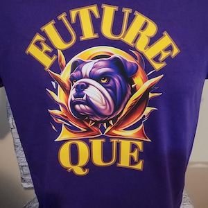 May include: Purple t-shirt featuring a bulldog graphic. The design includes the words "FUTURE" and "QUE" in yellow, arched above and below the dog's head. The bulldog is depicted in shades of purple, blue, and white.
