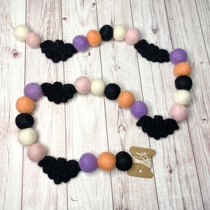 Puede incluir: Una guirnalda de Halloween con murci&eacute;lagos de fieltro negro, bolas de fieltro naranja, blanco, rosa y morado, y un carrete de hilo blanco.