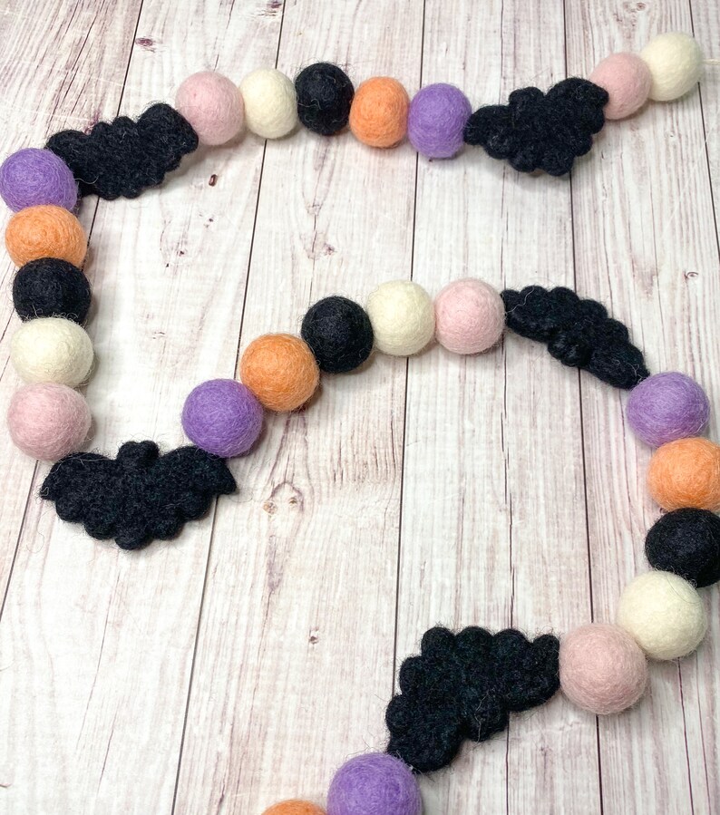 Puede incluir: Una guirnalda de Halloween con murci&eacute;lagos de fieltro negro, bolas de fieltro naranja, blanco, rosa y morado.