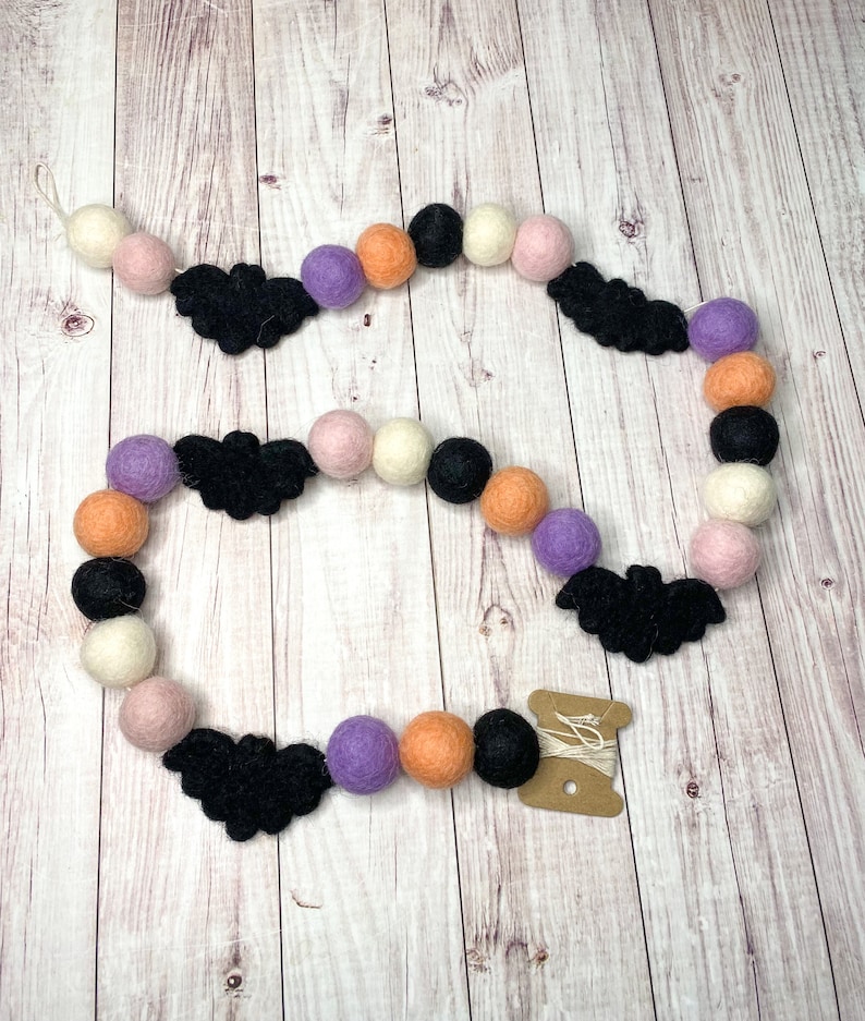 Puede incluir: Una guirnalda de Halloween con murci&eacute;lagos de fieltro negro, bolas de fieltro naranja, blanco, rosa y morado, y un carrete de hilo blanco.
