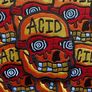 Può includere: Primo piano di diversi patch ricamati che raffigurano un teschio con occhi rossi che gocciolano e la parola "ACID" in lettere gialle. I patch sono di un vibrante arancione, rosso e giallo.