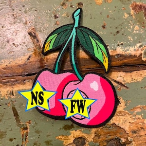 May include: Embroidered patch featuring a pair of pink cherries with green leaves and stems. Each cherry has a star-shaped graphic with the letters "NS" and "FW" in yellow. The patch has a black border.