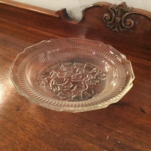 May include: A clear glass bowl with a decorative floral pattern. The bowl has a scalloped edge and is made of clear glass.