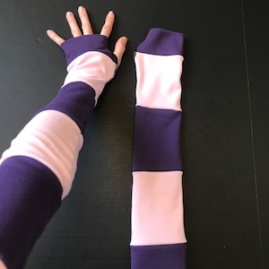 May include: A pair of striped arm warmers in pink and purple. The arm warmers are made of a soft, stretchy fabric and are perfect for keeping your arms warm in the cooler months.
