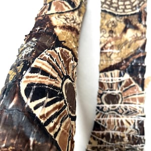 May include: Two long, narrow fabric strips featuring a textured, crinkled surface with a repeating abstract pattern in shades of brown, black, tan, and cream. The design includes circular motifs and geometric lines printed across the material.