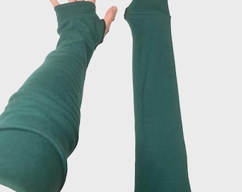 May include: A pair of dark forest green arm warmers featuring a thumb hole design. The fabric is a solid, smooth material that extends from the wrist up to the forearm. One arm warmer is shown worn on an arm, while the other lies flat beside it.