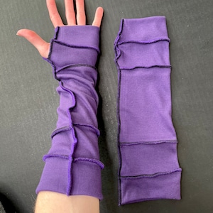 May include: A pair of purple arm warmers with black stitching. The arm warmers are made of a soft, stretchy fabric and have a unique, layered design.