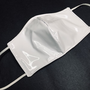 May include: A white face mask made of shiny, glossy fabric. The mask has elastic ear loops.
