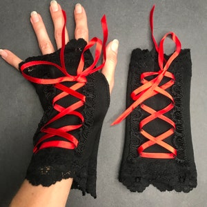 May include: A pair of black lace fingerless gloves with red satin ribbon lacing. The gloves are tied at the wrist with a bow.