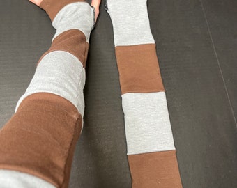 May include: A pair of arm warmers featuring a color-blocked pattern of alternating horizontal stripes in brown and heather gray fabric. One arm warmer includes a thumb hole opening at the top, while the other is a simple tube design.