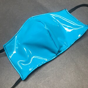 May include: A bright cyan face mask made of a glossy, patent-like material. The mask features a central vertical seam for shaping and is finished with black stitched edges. Two black elastic ear loops are attached to the sides of the mask.