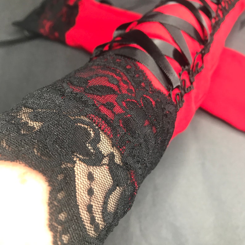 May include: Red and black lace arm warmers with black ribbon lacing. The arm warmers are made of a soft, stretchy fabric and have a delicate lace design.
