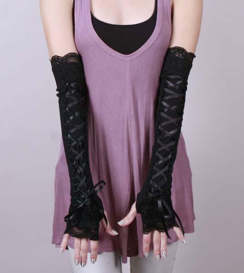 May include: A pair of black fingerless arm warmers featuring a lace trim at the top and bottom edges. The sleeves are designed with a crisscross ribbon lacing detail running down the center, finished with a small bow at the wrist area.