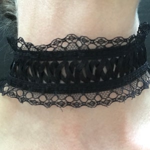 May include: A black lace choker with a delicate, scalloped edge. The choker features a woven design in the center.