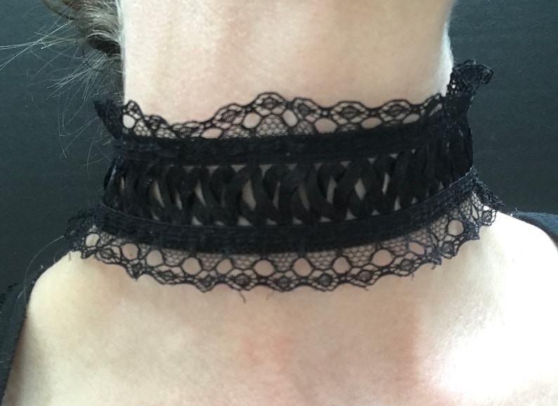 May include: A black lace choker with a delicate, scalloped edge. The choker features a woven design in the center.